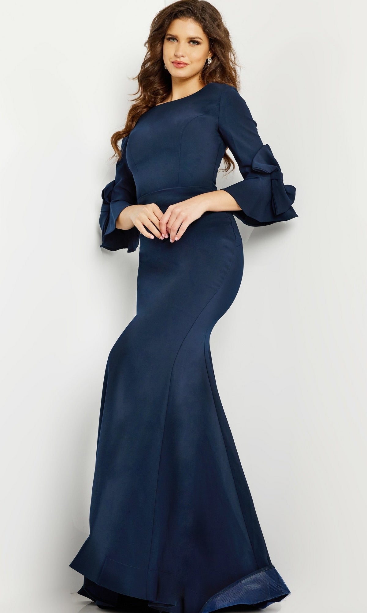 A woman wears the Long Formal Jovani Dress 09776, a dark blue, floor-length gown with ruffled long sleeves, standing against a plain light background.
